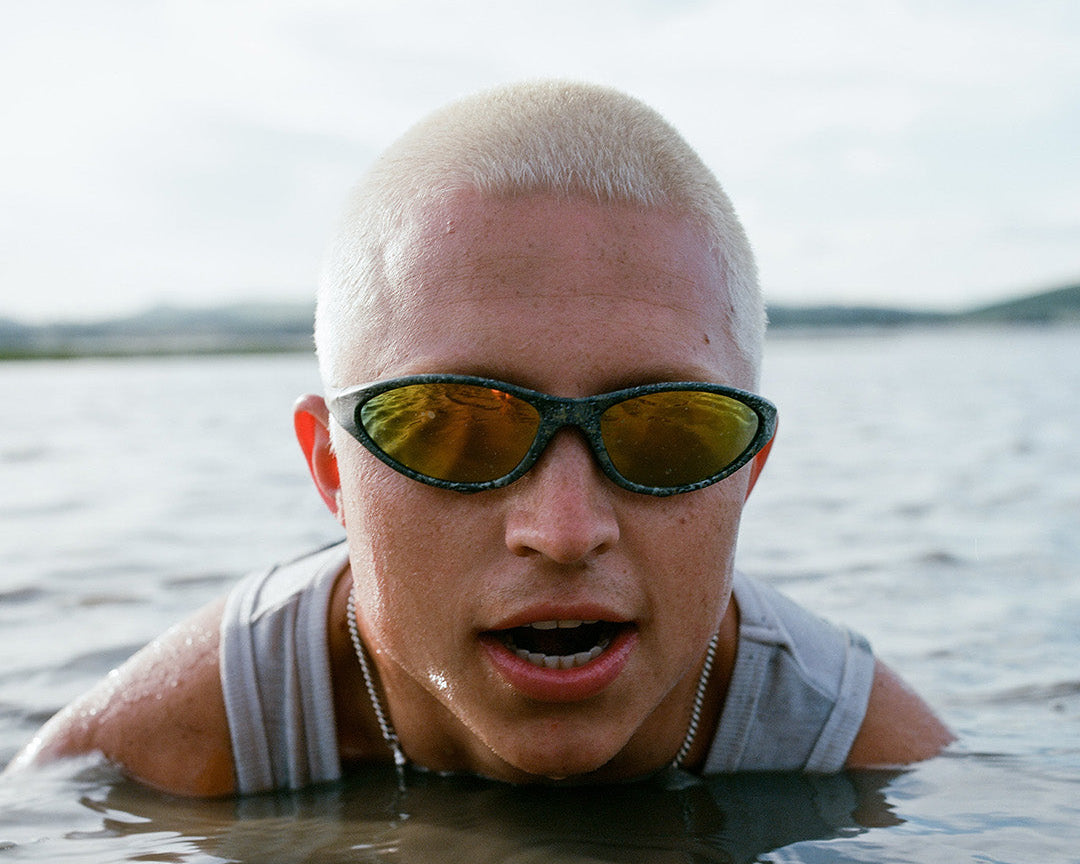 Australian person wearing croc eye aim sunnies sunglasses and a gray shirt partially submerged in water 